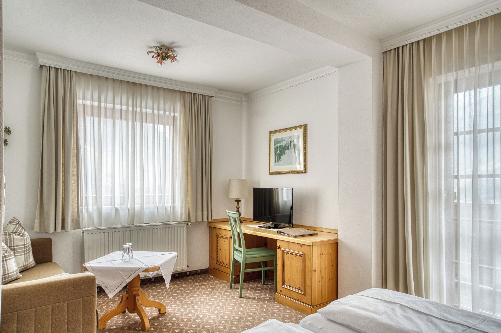 Ett hotellrum med en säng, ett skrivbord med en stol, en tv och ett fönster med gardiner.