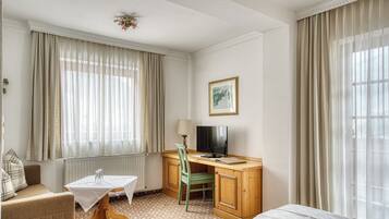 Ett hotellrum med en säng, ett skrivbord med en stol, en tv och ett fönster med gardiner.
