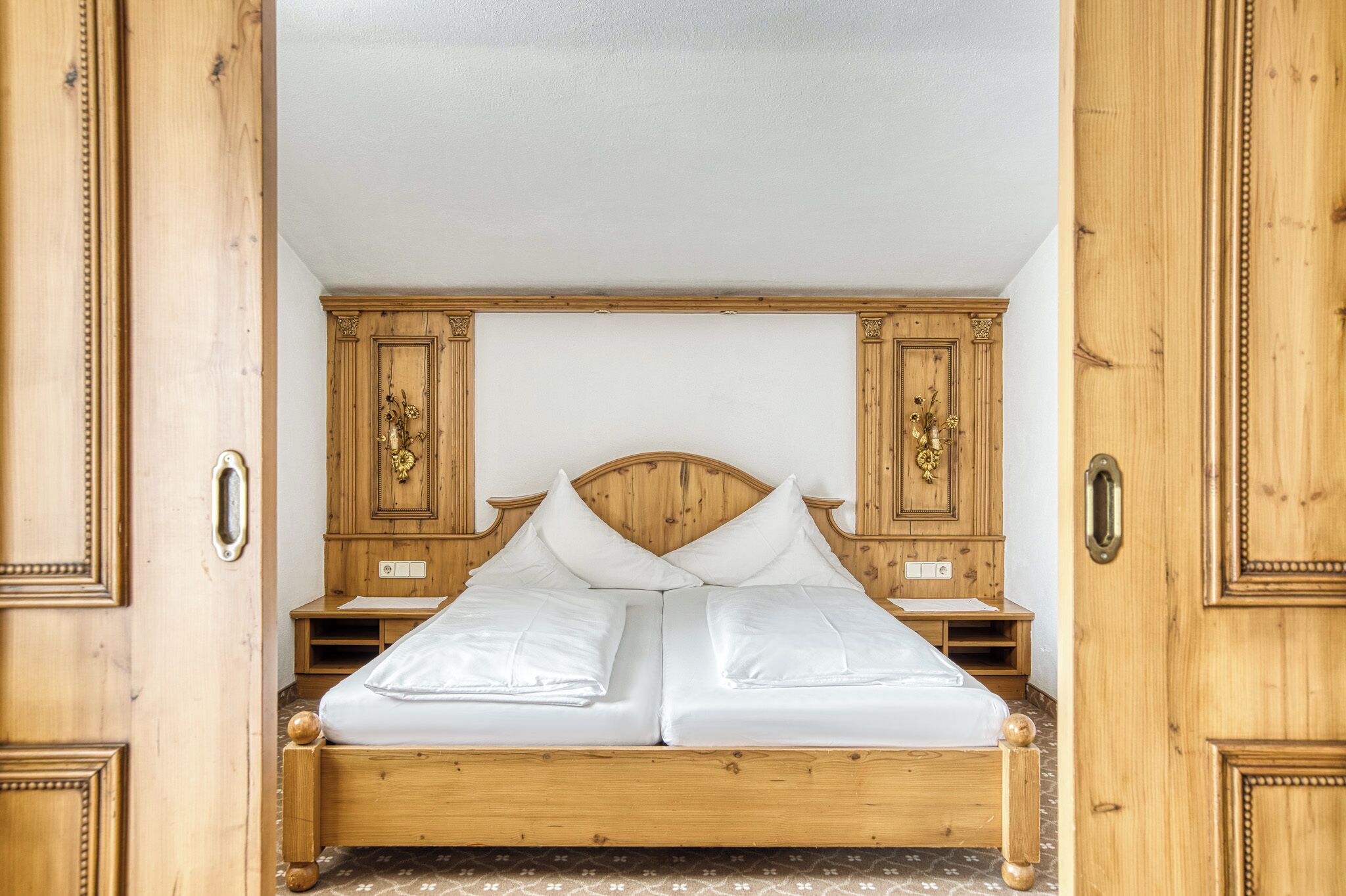 Ein hölzernes Himmelbett mit weißen Leinen, begleitet von Nachttischen aus Holz mit verzierten Griffen.