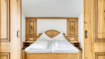Ein hölzernes Himmelbett mit weißen Leinen, begleitet von Nachttischen aus Holz mit verzierten Griffen.