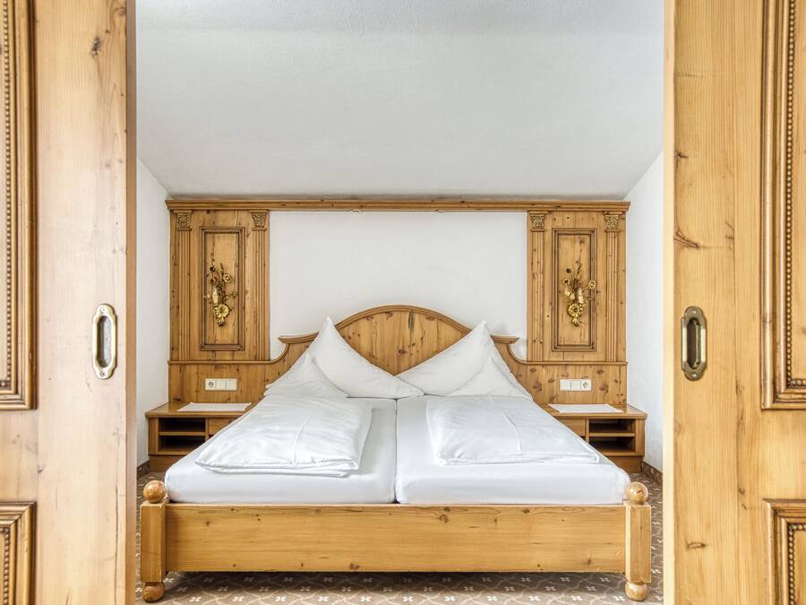Ein hölzernes Himmelbett mit weißen Leinen, begleitet von Nachttischen aus Holz mit verzierten Griffen.