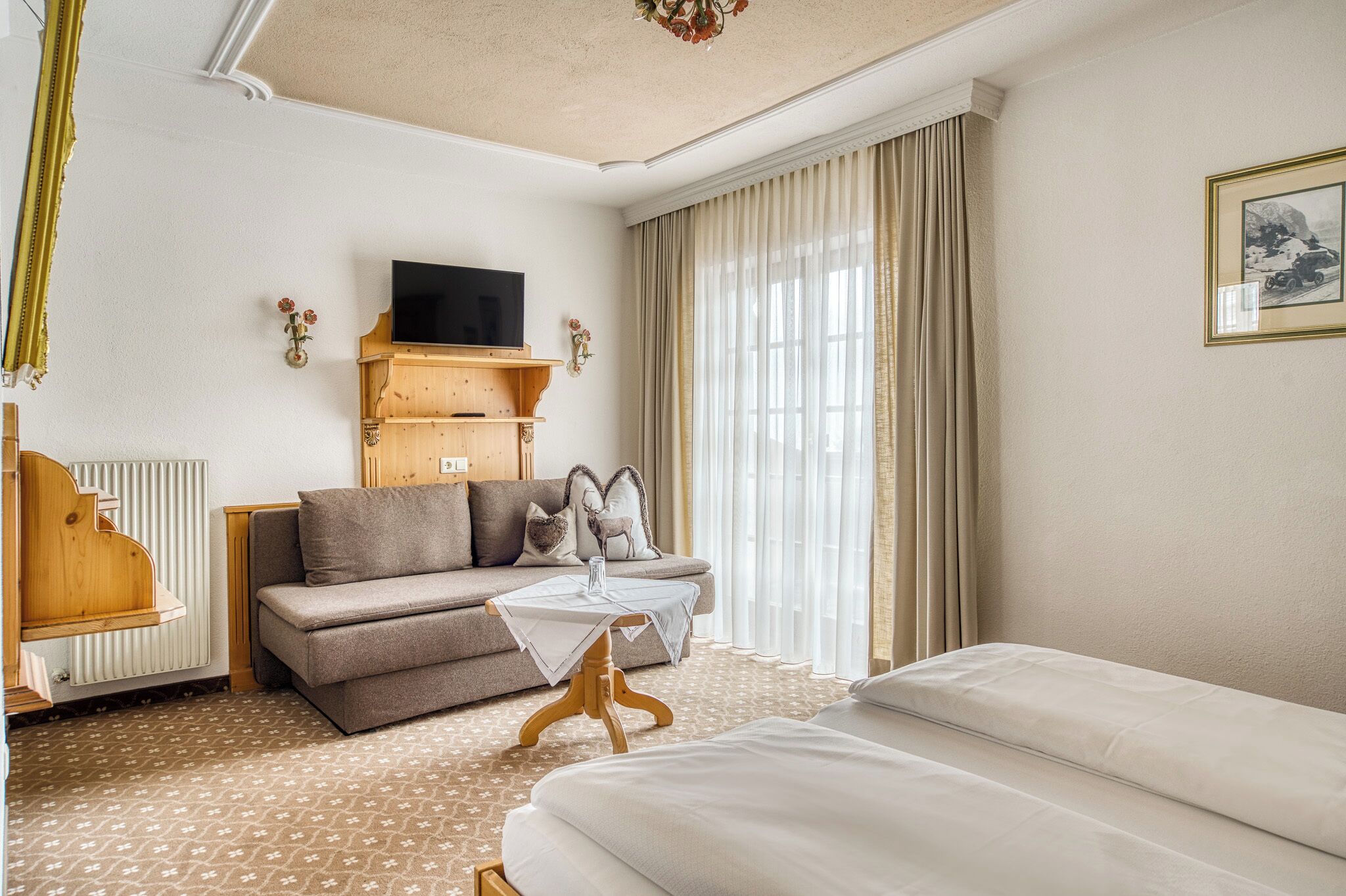 A hotel room with a sofa, a small table, a bed, a TV, and a radiator.