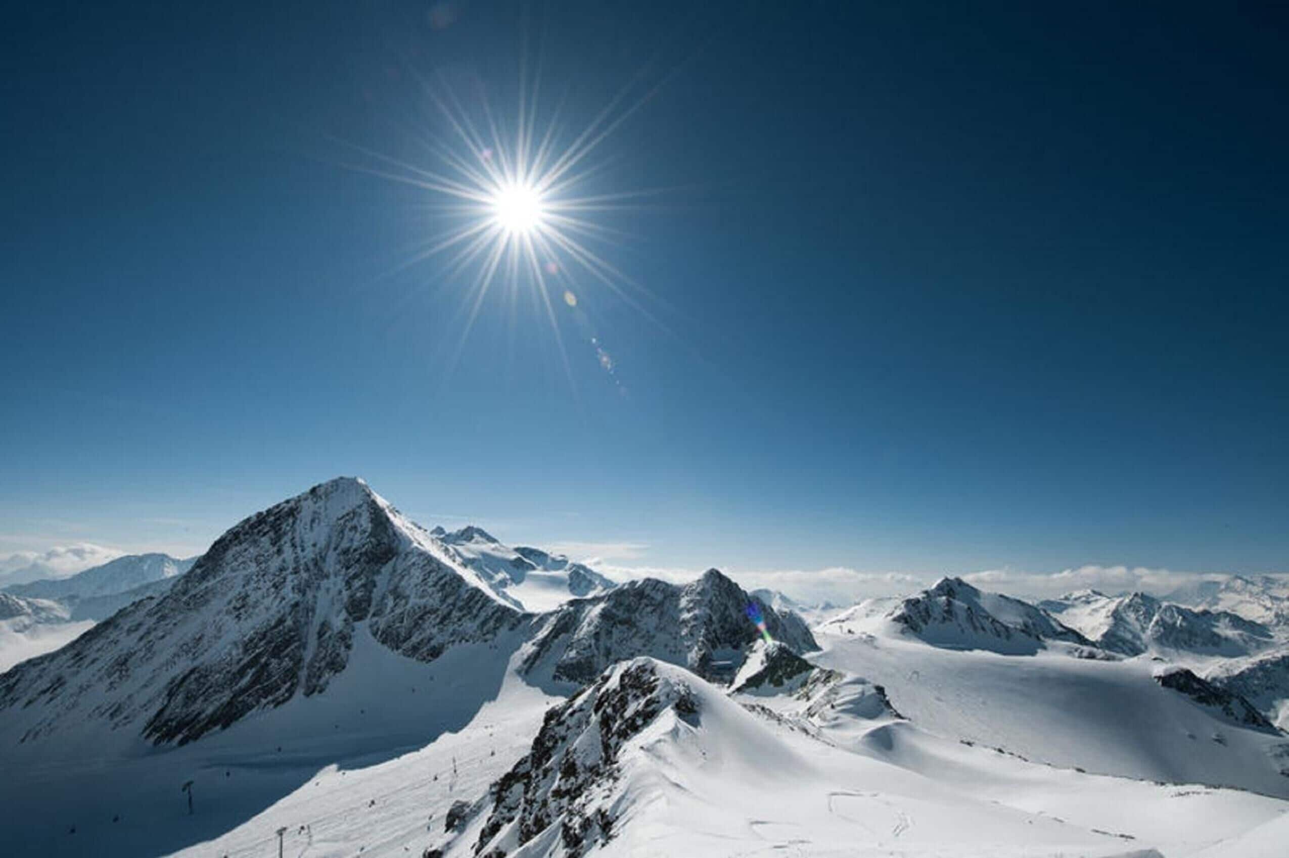 A snow-covered mountain landscape with a clear sky and the sun shining brightly.