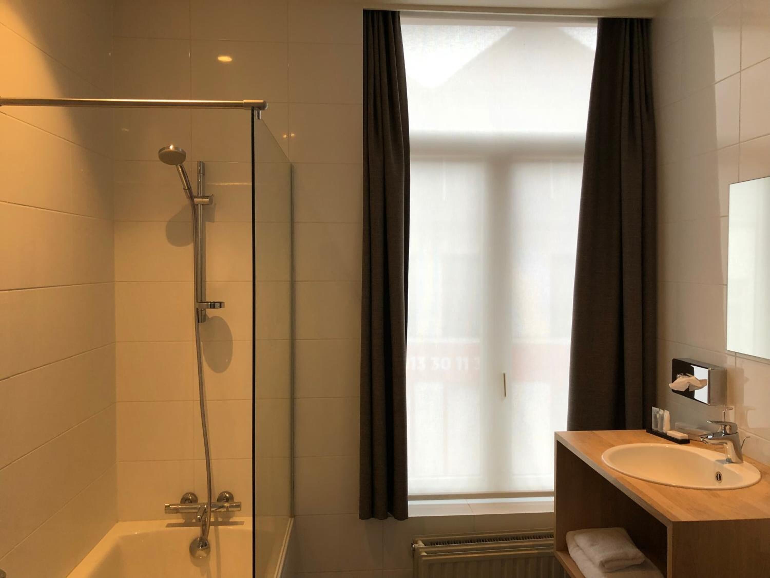 A modern bathroom with a glass-enclosed shower, a large window with curtains, and a wooden vanity with a sink.