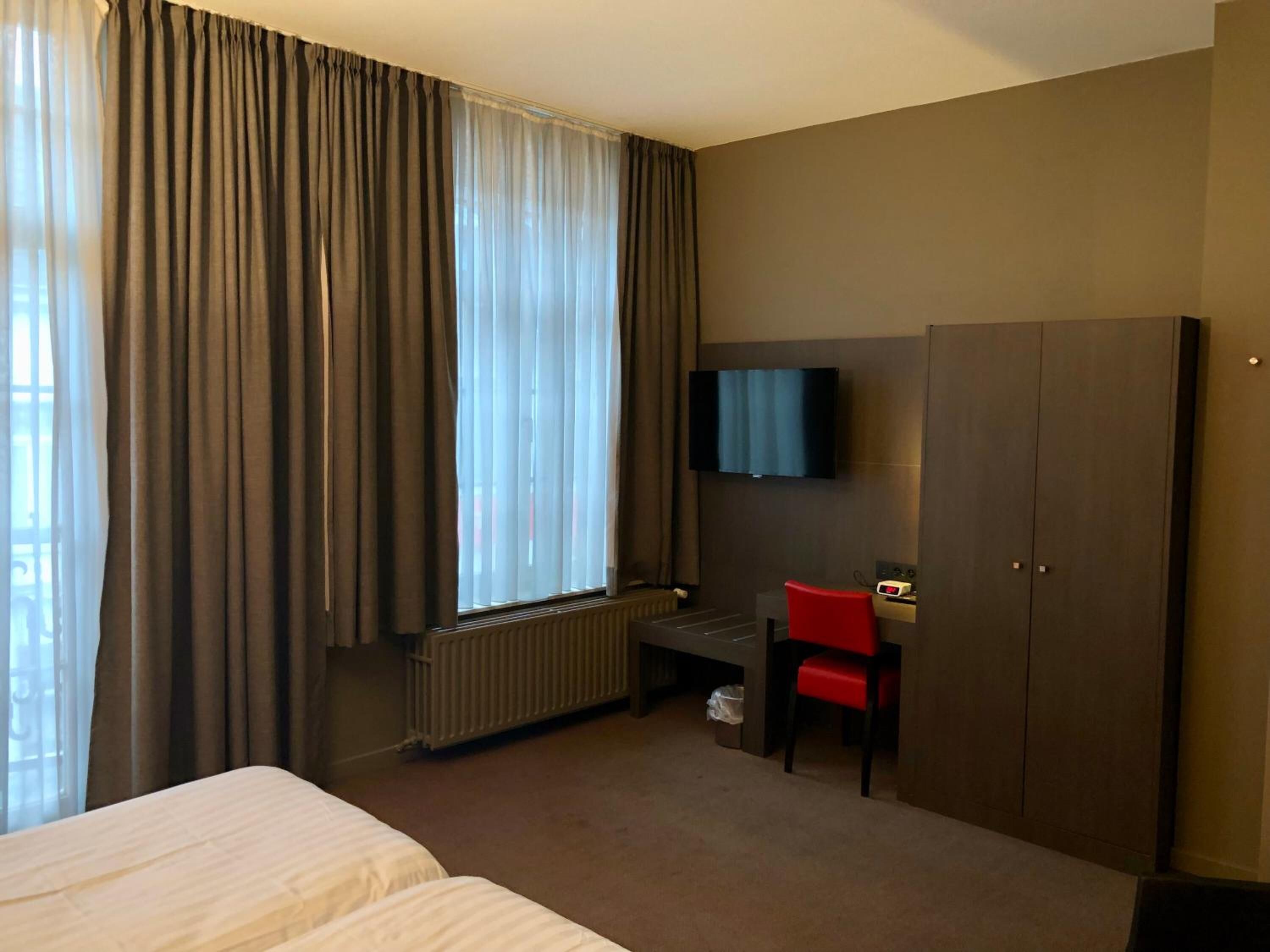 Una habitación de hotel con una cama, un escritorio, una silla, un televisor y un armario.