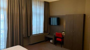 Una habitación de hotel con una cama, un escritorio, una silla, un televisor y un armario.
