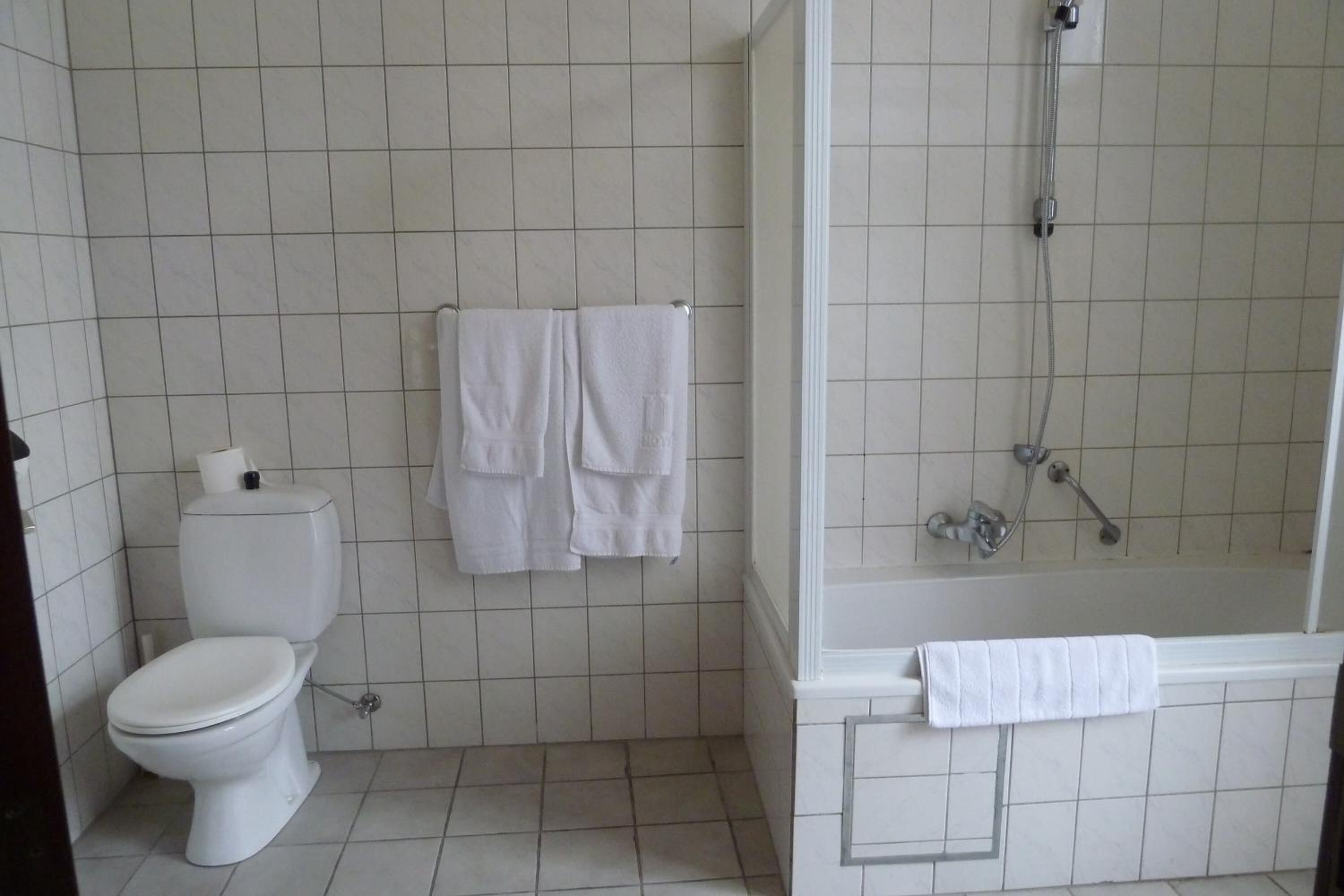 Un baño con inodoro, dos toallas blancas colgadas en la pared, una ducha con puerta de vidrio y una bañera.