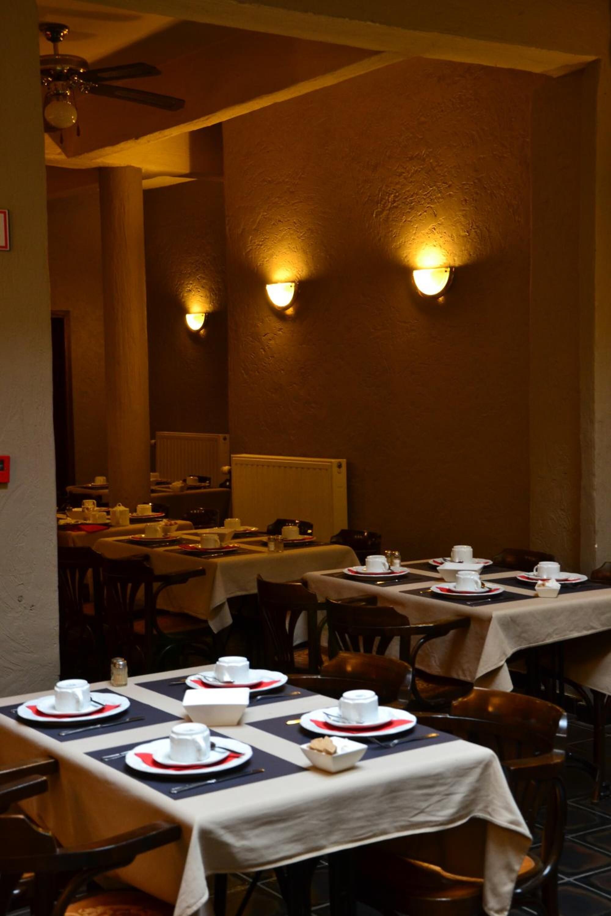 A restaurant with tables set for dining, featuring a ceiling fan and wall-mounted lighting.