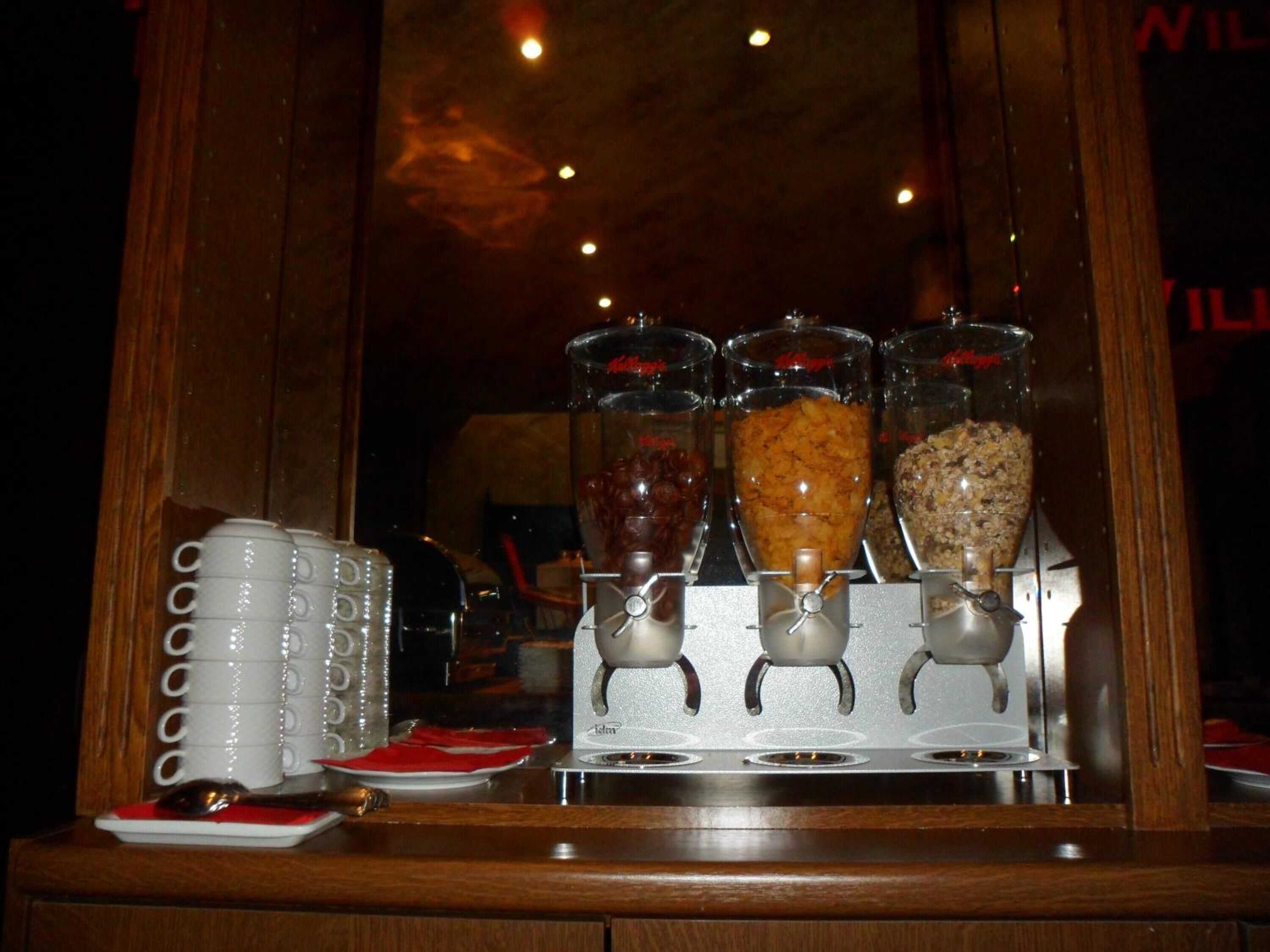 A breakfast bar with a coffee machine and three dispensers of different food items.
