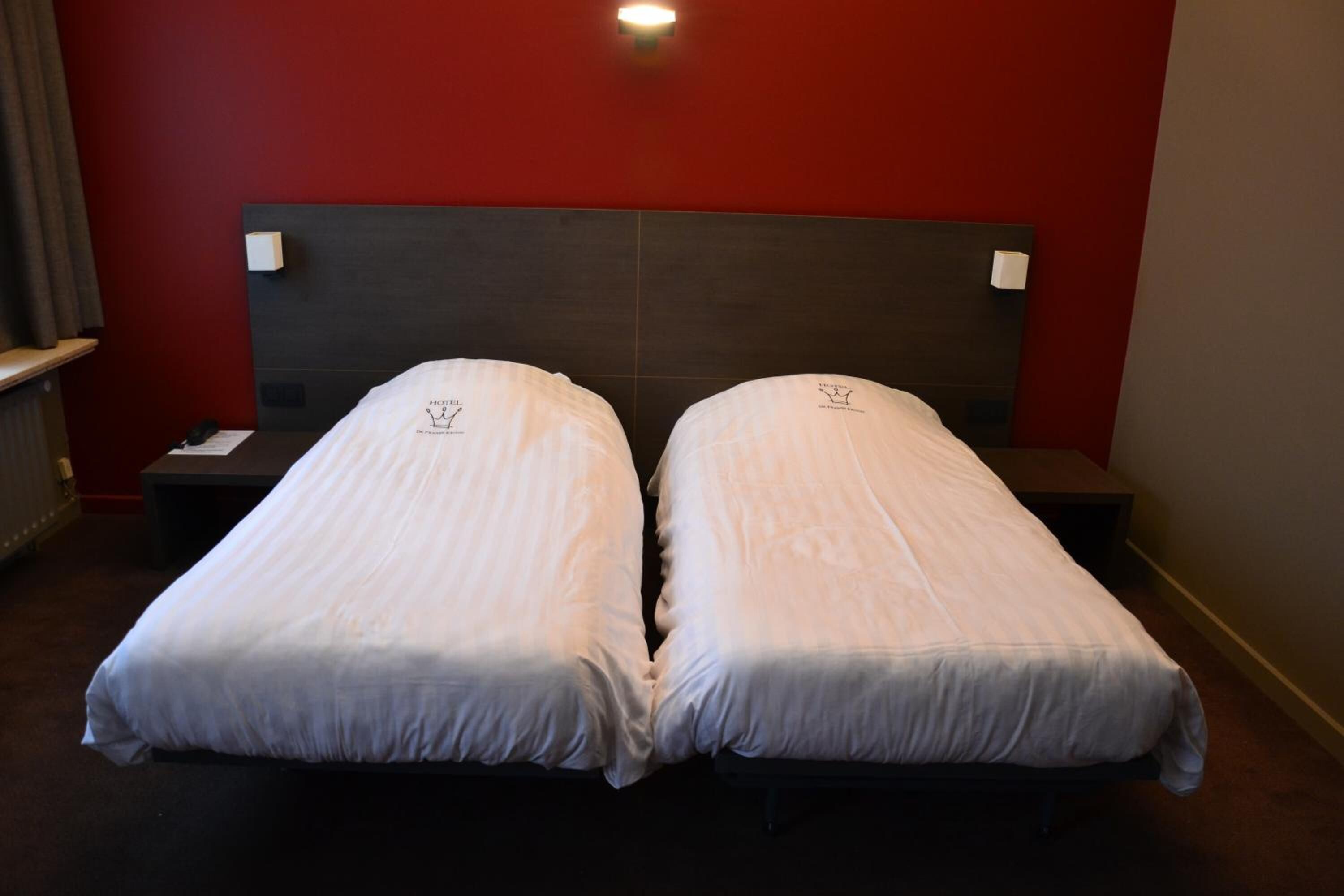 Quarto de hotel com duas camas de solteiro, cabeceira escura e parede de destaque vermelha.