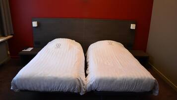 Quarto de hotel com duas camas de solteiro, cabeceira escura e parede de destaque vermelha.