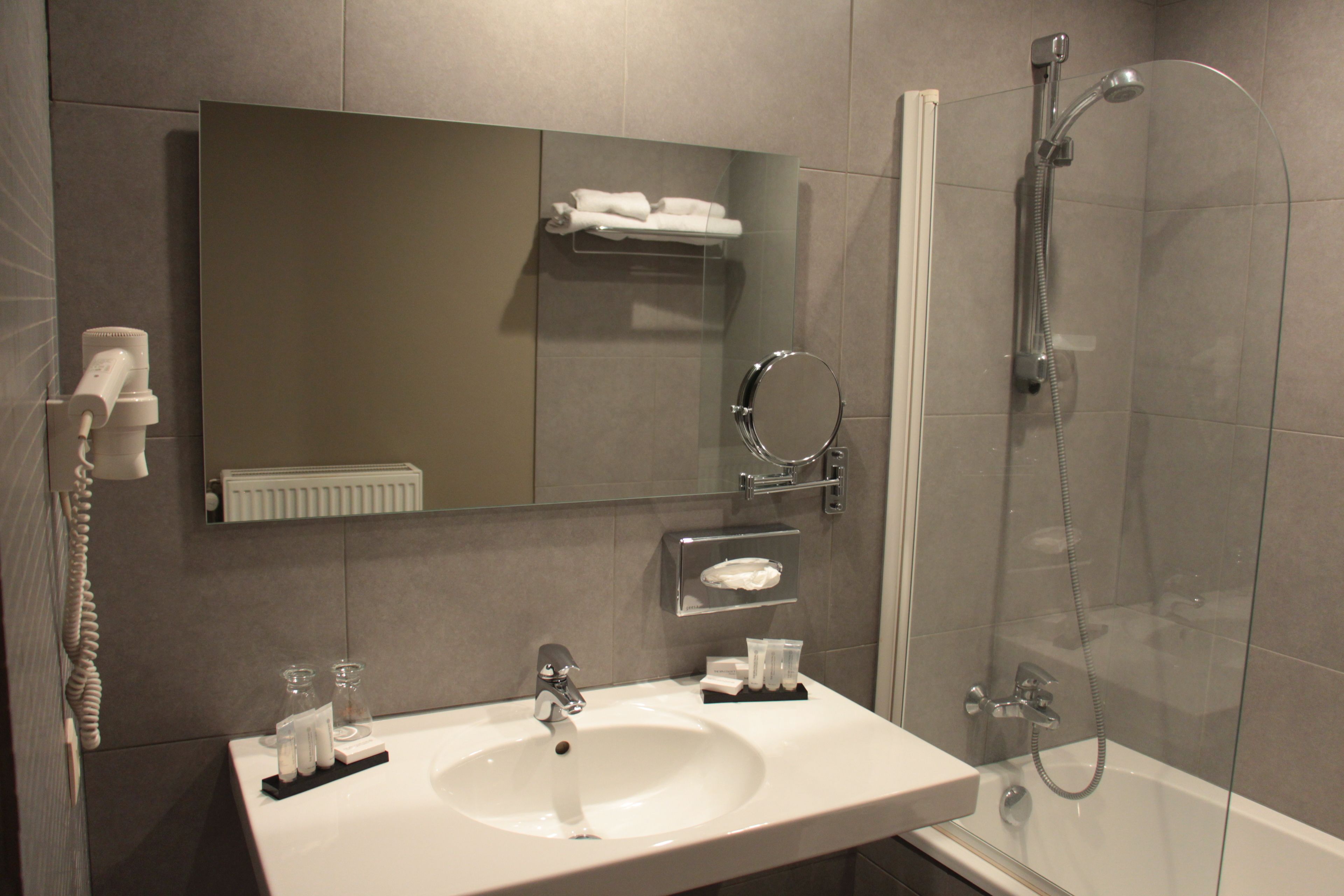 A modern bathroom with a large mirror, a sink, a shower, and a towel rack.