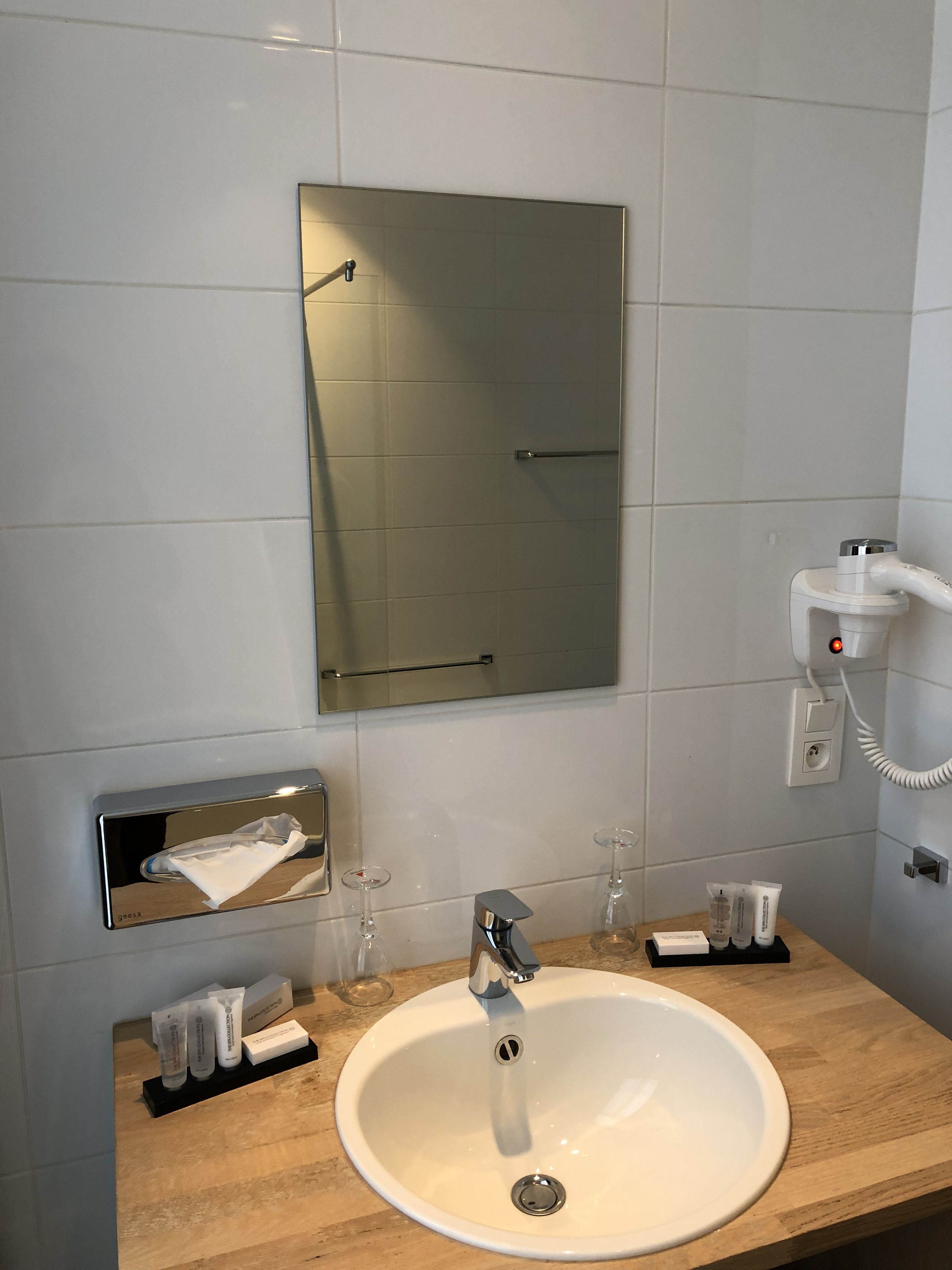 Un baño con un lavamanos blanco, un espejo y un perchero para toallas.