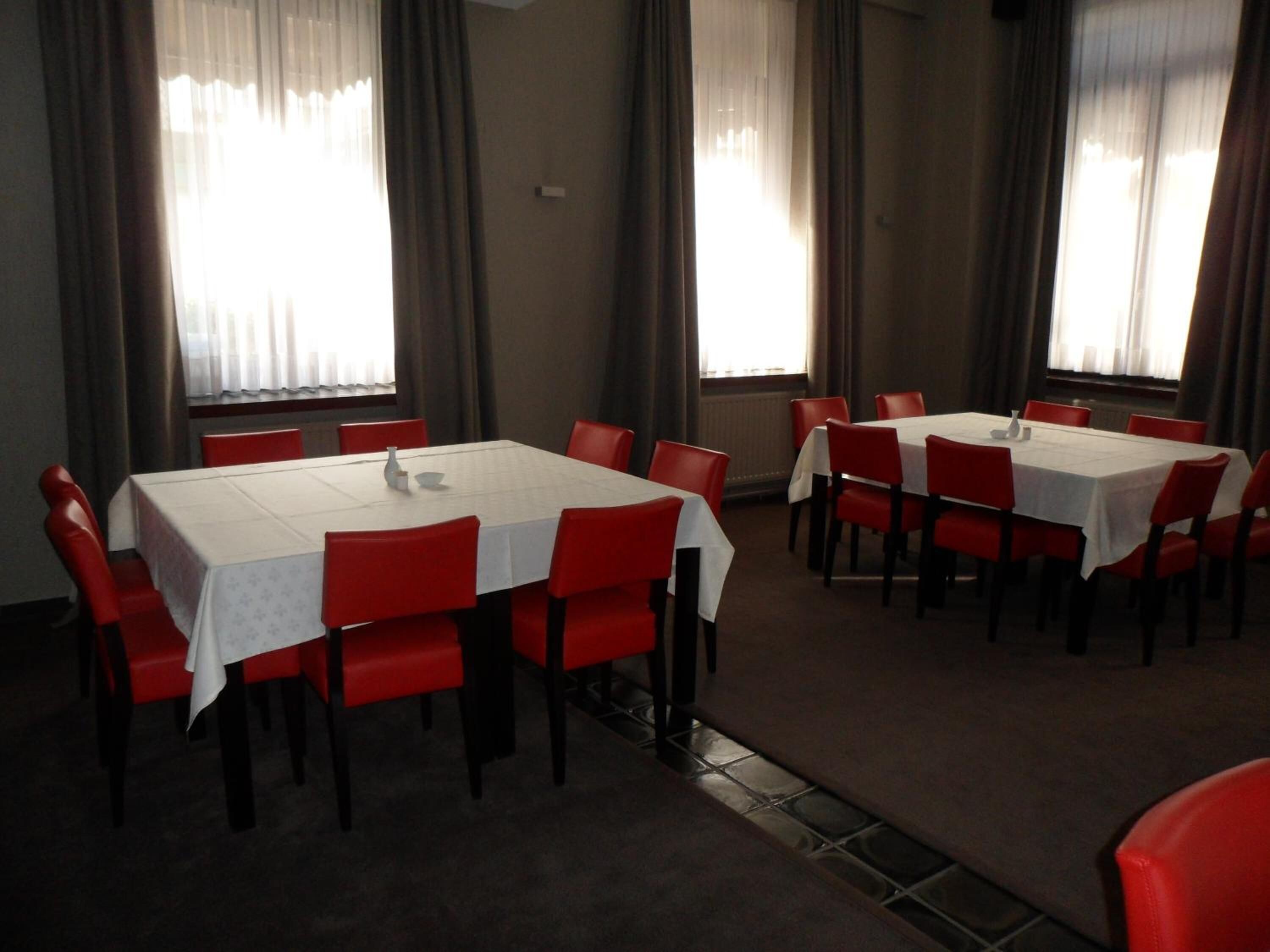 Un espace repas comprenant plusieurs tables et chaises, disposées dans une pièce spacieuse dotée de grandes fenêtres et de rideaux.