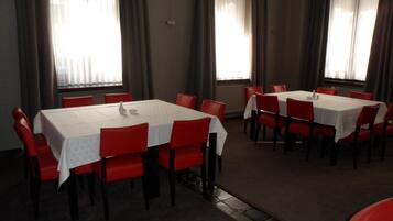 Un espace repas comprenant plusieurs tables et chaises, disposées dans une pièce spacieuse dotée de grandes fenêtres et de rideaux.