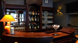A bar area with a round wooden counter, a lamp, a wine glass, and shelves stocked with bottles and glasses. - Hotel De Franse Kroon (Diest)