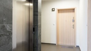 Un corridoio con un ascensore moderno, una porta in legno e un pavimento piastrellato.