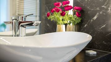 Un baño con un lavabo blanco tipo recipiente, grifo cromado y un florero con flores rosadas sobre la encimera.