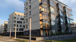 Un edificio residenziale moderno a più piani con balconi, un vialetto lastricato e un'area verde curata.