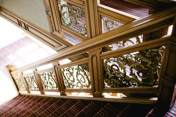 A wooden staircase with ornate metal railings and patterned floor tiles.