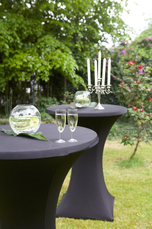 Dos mesas redondas con superficie negra, cada una con una copa de vino blanco y un cuenco de vidrio decorativo. En la mesa al fondo se encuentra un candelabro con velas.