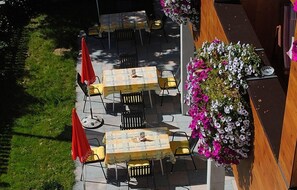 An outdoor patio with tables and chairs, surrounded by greenery and a wooden structure. - Gasthof Kaiserblick (Breitenbach am Inn)