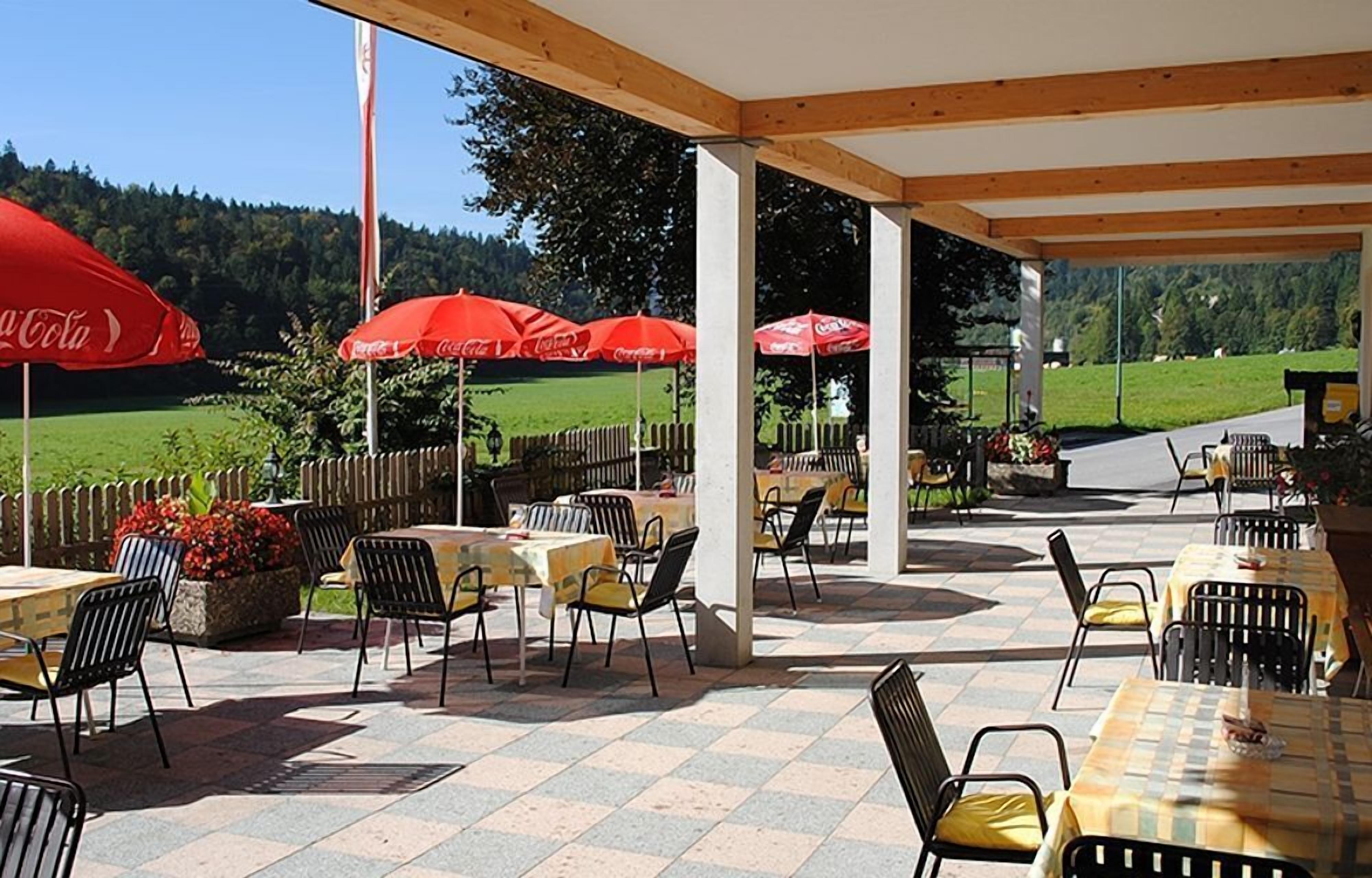 An outdoor patio area with tables and chairs, red umbrellas, and a view of a green landscape.