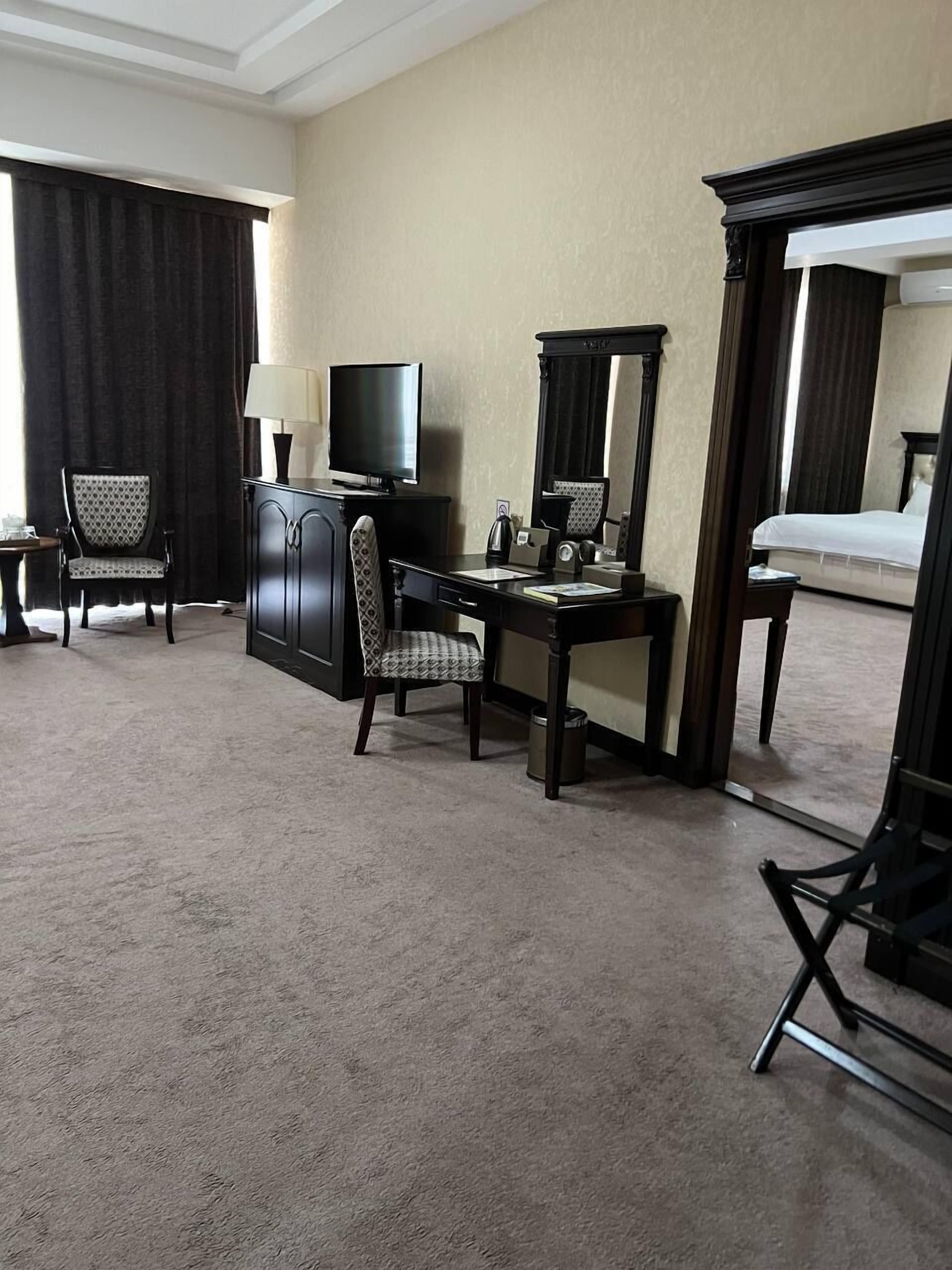 Una habitación de hotel con escritorio, dos sillas, televisor, cama y un espejo grande.