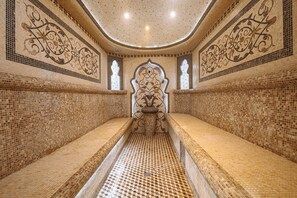 Une pièce dotée d’un sol carrelé, d’une colonne centrale agrémentée d’un élément décoratif et de murs ornés de motifs complexes en carreaux.