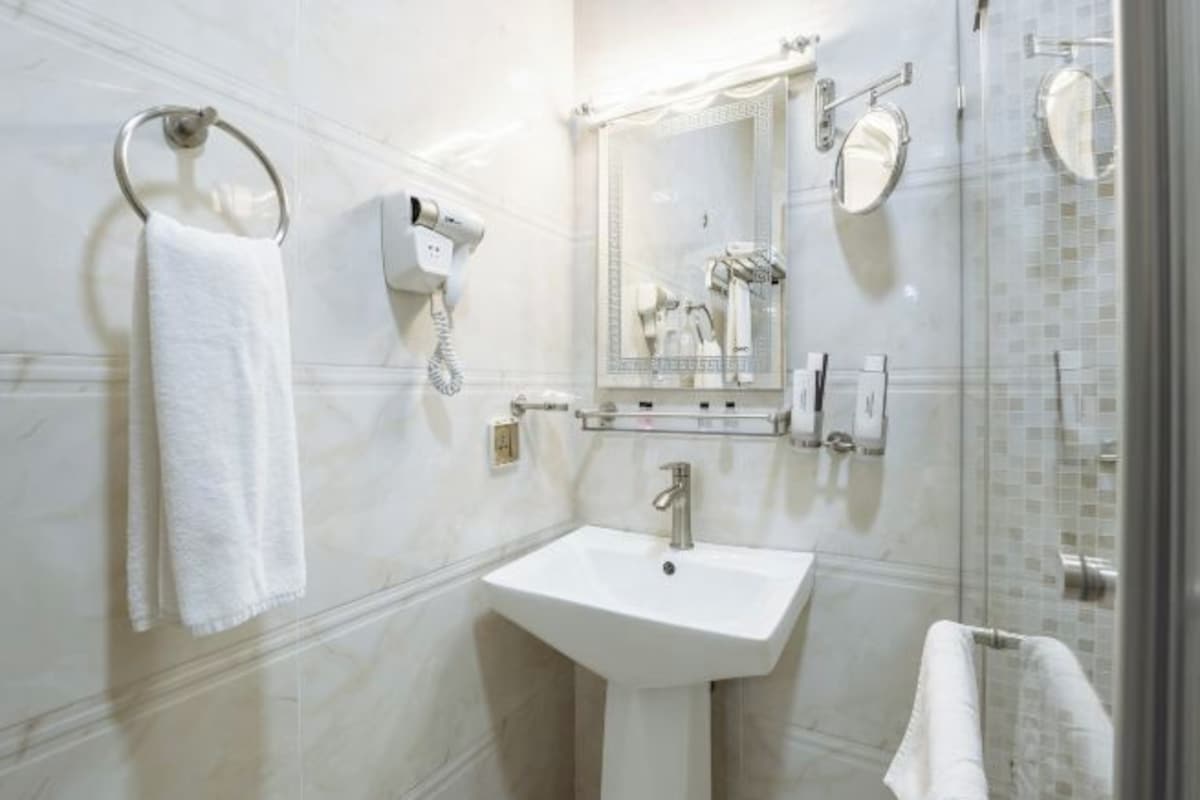 Ein modernes Badezimmer mit Waschbecken in Weiß, einem Handtuchhalter, einem Fön und einer Duschkabine aus Glas.