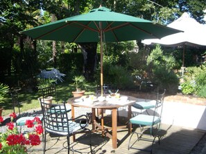 An outdoor patio with a wooden table and chairs, a green umbrella, and potted plants. - Chambres d'hôtes Les Douves (Saint-Thomas)