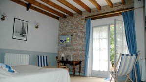 Ein Schlafzimmer mit einem Bett, einem Schreibtisch, einem Stuhl, einem Fenster mit Vorhängen und einer Ziegelwand.