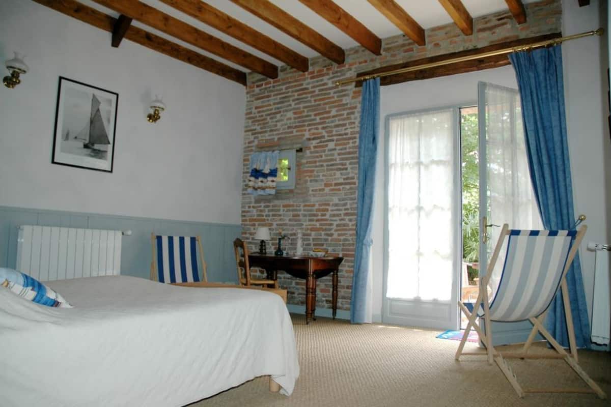Une chambre à coucher avec un lit, un bureau, une chaise, une fenêtre avec des rideaux et un mur en briques.