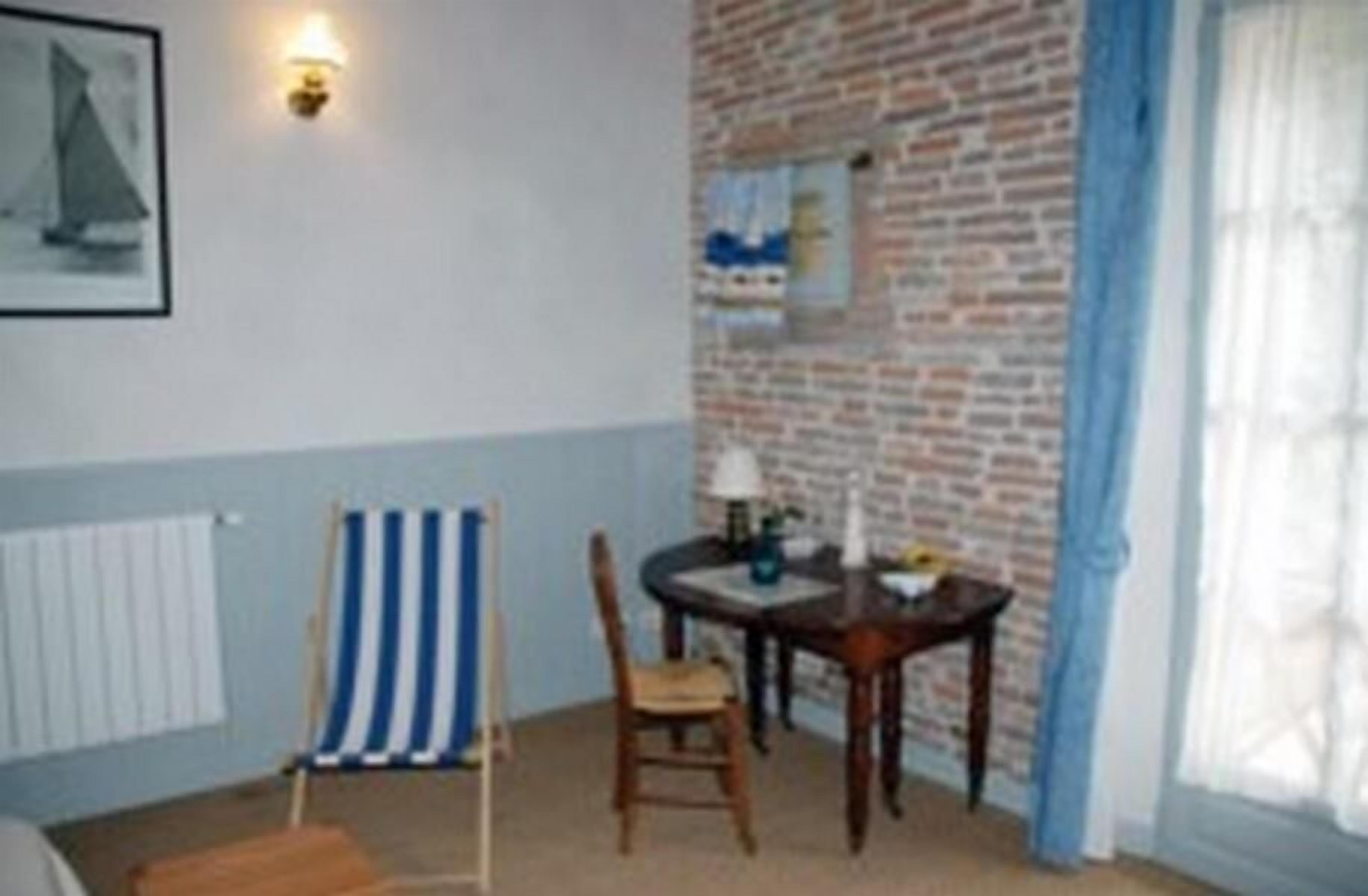 A room with a brick wall, a small table with a chair, a striped beach towel, and a framed picture on the wall.