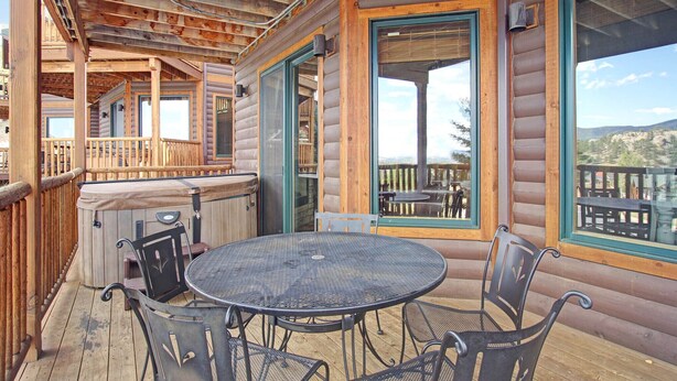 A wooden deck with a round metal table and chairs, large windows, and a hot tub.