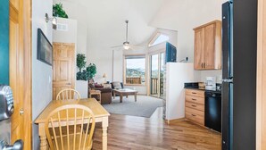A compact kitchen with wooden cabinets, a dining area with a table and chairs, a ceiling fan, and a view through a large window. - Teepee Mountain 12a 2 Bedroom Condo by RedAwning (Estes Park)