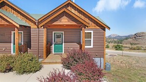 A log cabin with a green door, a small porch, and a view of the surrounding landscape. - Comanche Peak 39 2 Bedroom Condo by RedAwning (Estes Park)