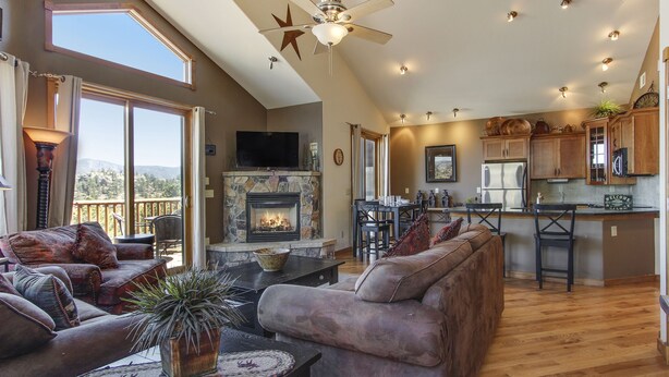 A spacious living area with a fireplace, comfortable seating, and a kitchen area with wooden cabinets and a bar. - The Twin Owls 21a 2 Bedroom Condo by RedAwning (Estes Park)
