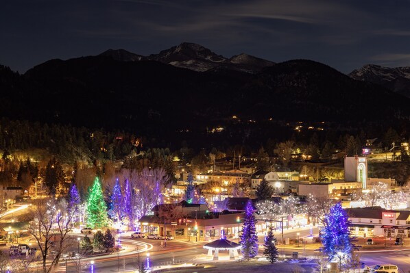 Un pueblo con árboles de Navidad iluminados y montañas al fondo.