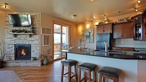 Une cuisine moderne avec une cheminée en pierre, des tabourets de bar en bois et un grand îlot central.