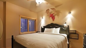 Un lit bien fait, avec du linge de lit blanc, une tête de lit en bois et une tête d’élan empaillée accrochée au mur.