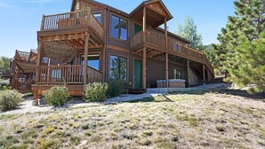 Une cabane en bois à plusieurs étages, dotée de balcons et de grandes fenêtres, entourée d’une végétation clairsemée et d’arbres.