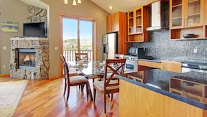 A modern kitchen with a stone fireplace, wooden cabinets, and a large island. - Mount Cairns 16a 2 Bedroom Condo by RedAwning (Estes Park)