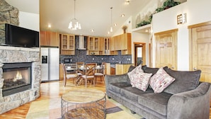 A modern living room with a fireplace, grey sofa, and a dining area with wooden chairs. - Mount Cairns 16a 2 Bedroom Condo by RedAwning (Estes Park)