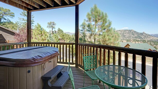 Une terrasse en bois avec un jacuzzi, une table et des chaises, offrant une vue sur un paysage montagneux.