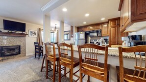 A modern kitchen with granite countertops, wooden cabinets, a built-in oven, and a flat-screen TV mounted above the fireplace. - Horizons 4 165 Updated Condo, Walk to Town, On Shuttle Route to Lodges by RedAwning (Mammoth Lakes)