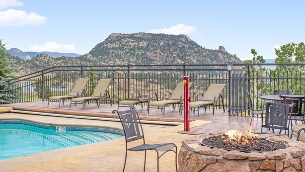 A pool area with lounge chairs and a fire pit, surrounded by a deck and a mountain view.