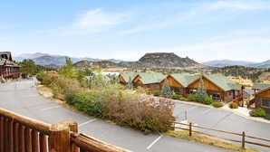 A row of log cabins with a mountain view, a parking lot, and a wooden fence.