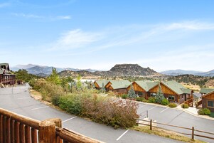 Filas de cabañas de madera con vista a la montaña, un estacionamiento y una cerca de madera.