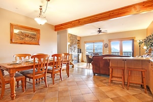 Un comedor con sillas y una mesa de madera, una cocina con barra de madera y vistas a montañas a través de amplios ventanales.